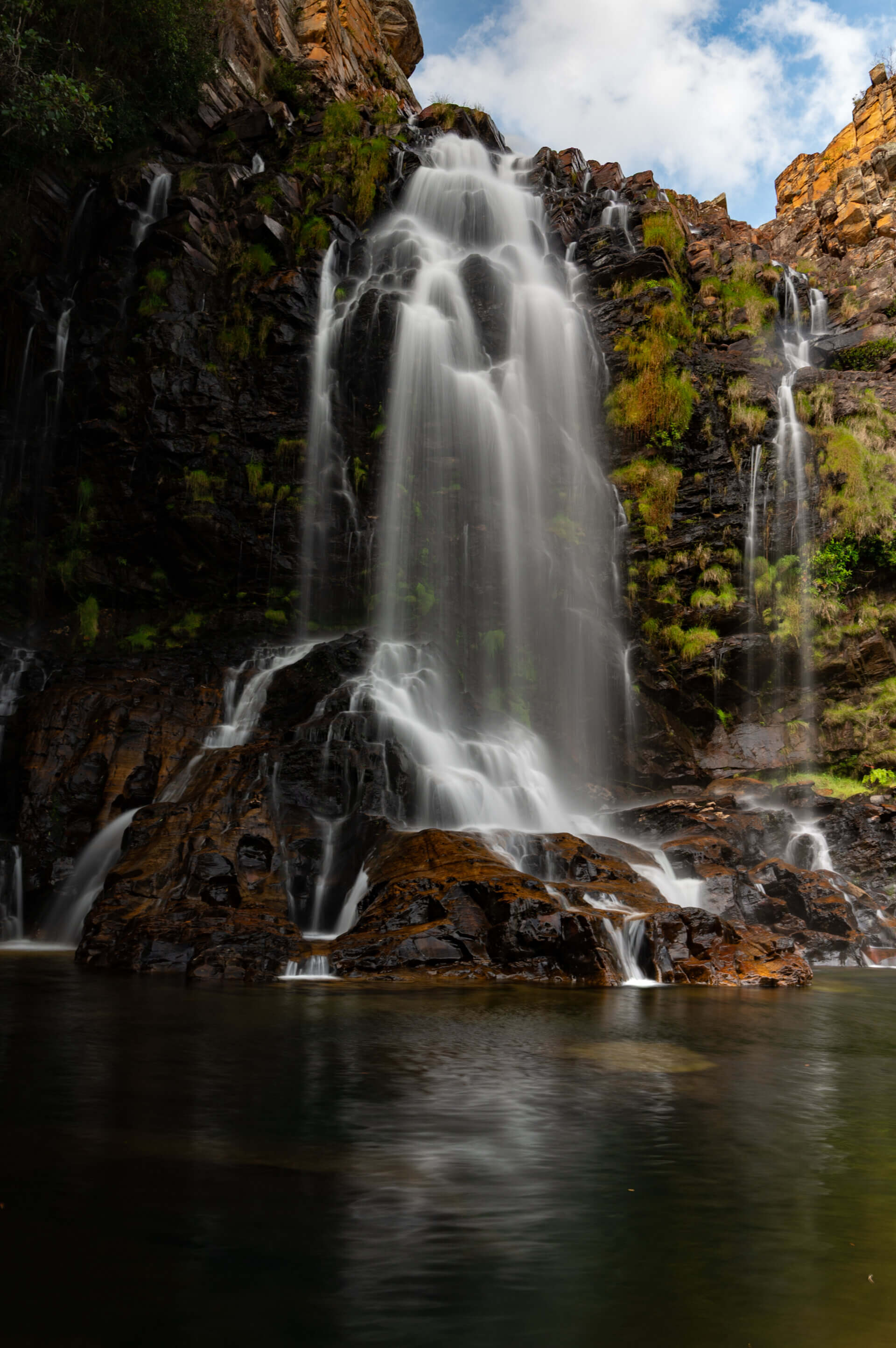 Long-exposure waterfall cascading over orange cliffs into a still pool in Brazil