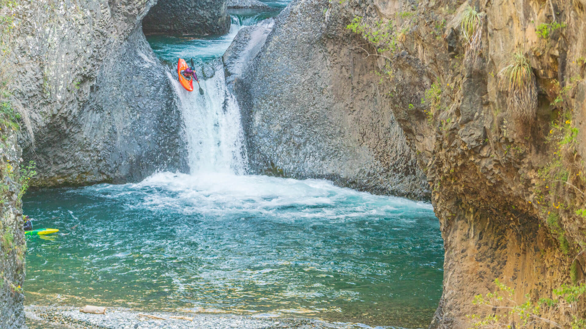 Whitewater kayaker launching off a waterfall into a turquoise pool in Chile