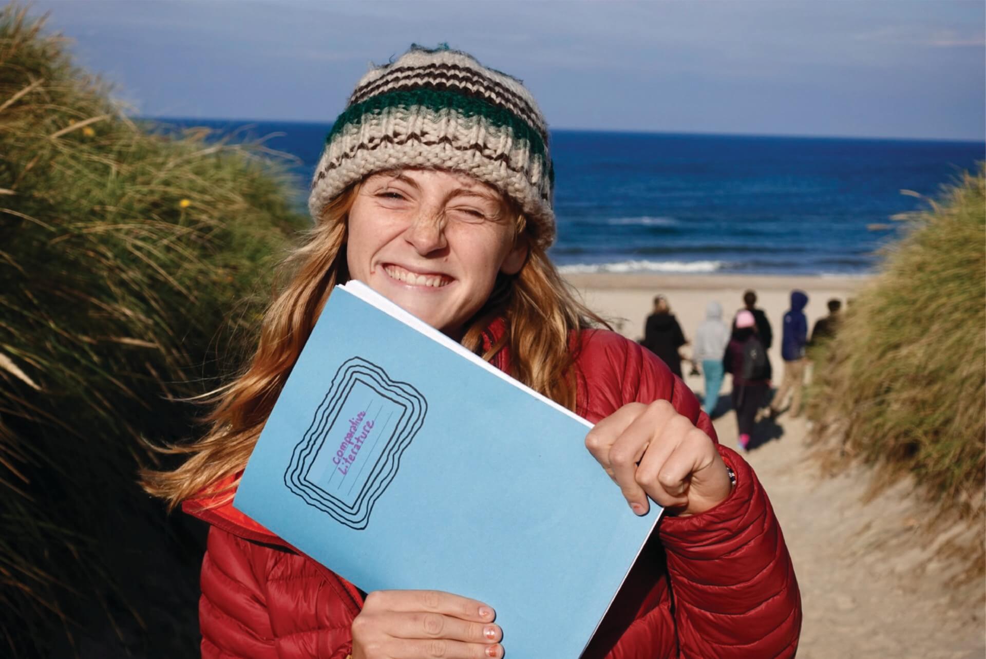 Student holding up comparative literature notebook and smiling.