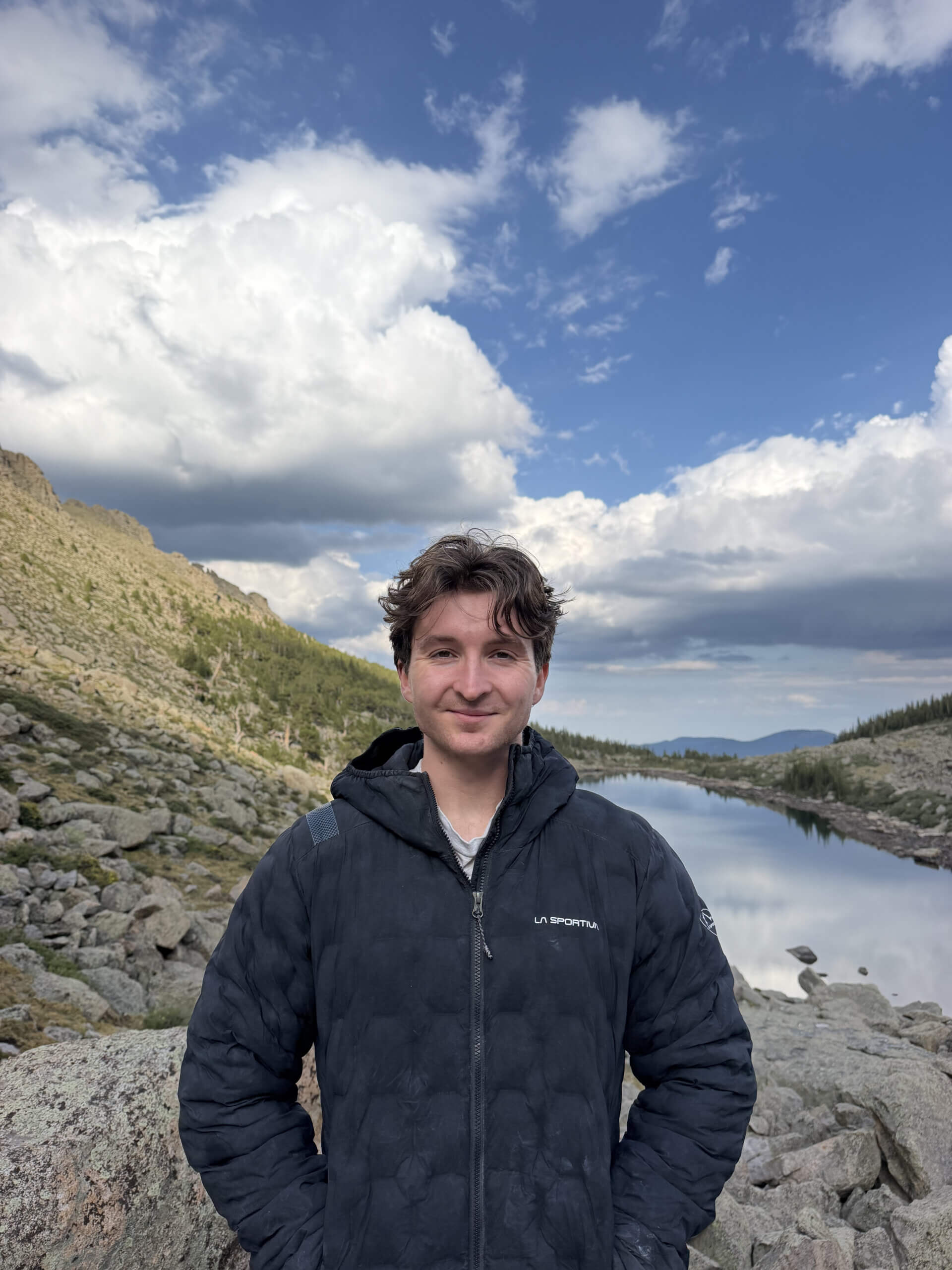Man standing by mountain lake under dramatic clouds