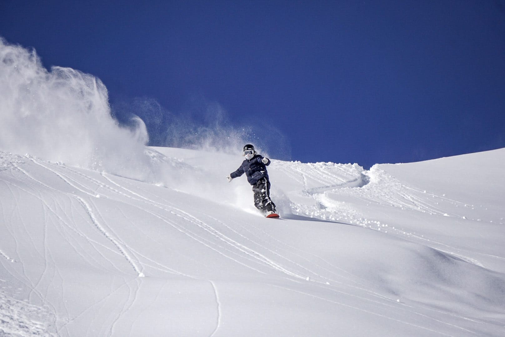 Snowboarder riding fresh powder under a deep blue sky