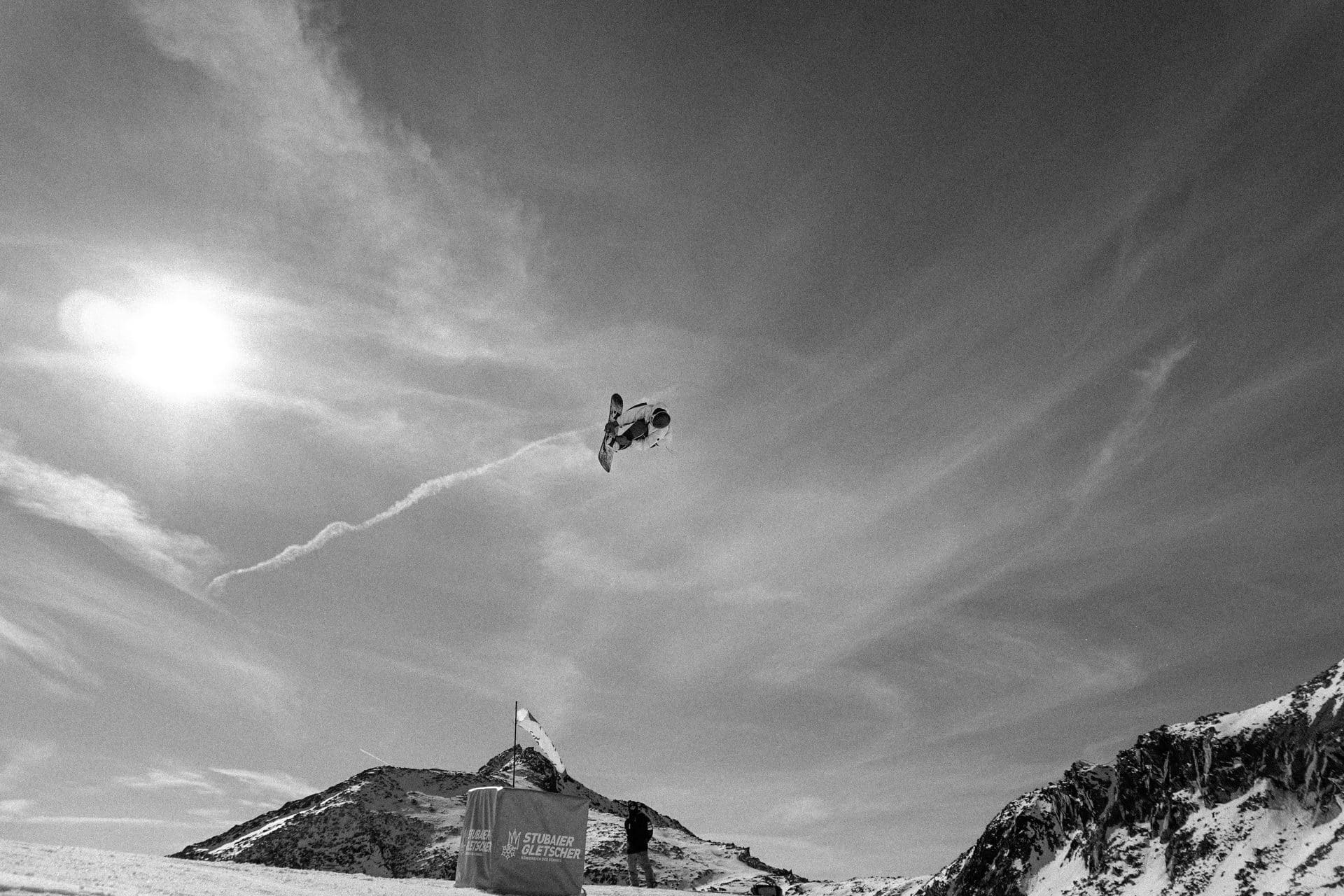 Black-and-white shot of a snowboarder high in the air against the sun
