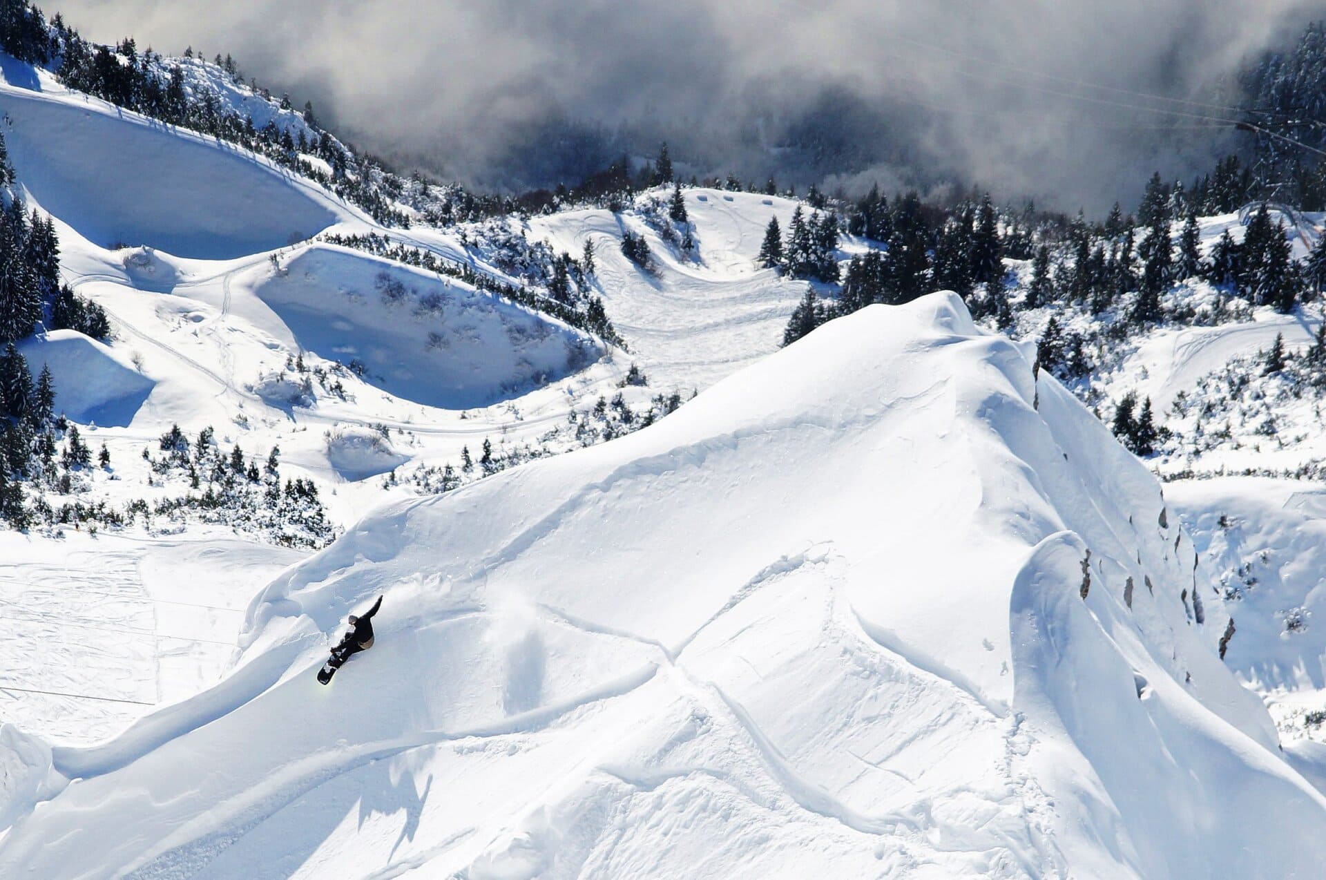 Snowboarder riding a wide freeride bowl below jagged peaks