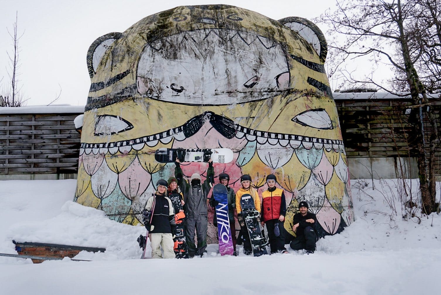 Snow Sports team posing with their boards in front of a painted tiger building
