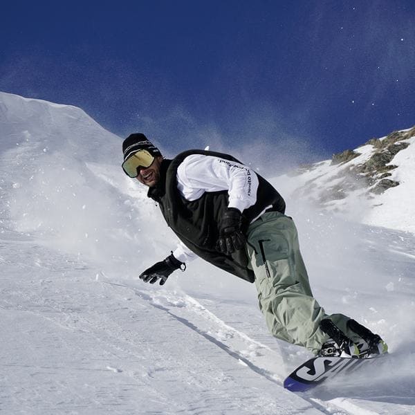 Snowboarder carving through spraying snow under a deep blue sky